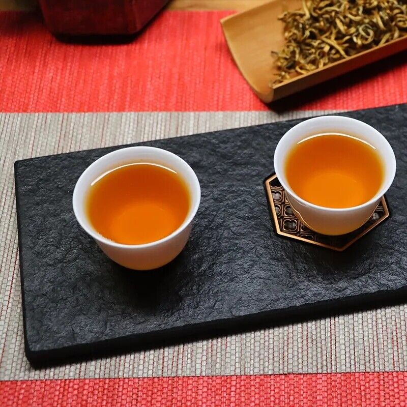 A glass cup filled with clear, brassy golden orange Dian Hong black tea infusion.